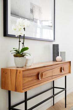 a vase with flowers on top of a wooden table in front of a framed photo