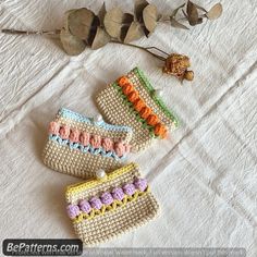 three crocheted purses sitting on top of a white sheet next to dried leaves