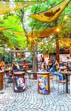 many people are sitting at tables under the shade umbrellas in an outdoor cafe area