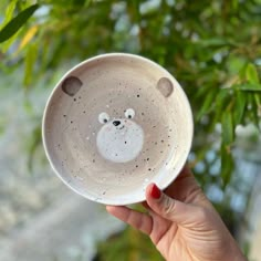 a hand holding a white bowl with a bear face on it