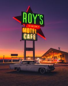 an old car is parked in front of a motel at night with the neon sign for roy's