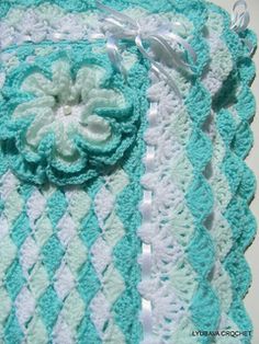 a crocheted blanket with a flower on the center and white trim around it