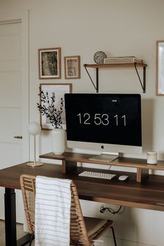 a desk with a computer on it and pictures hanging above the monitor, along with a wicker chair