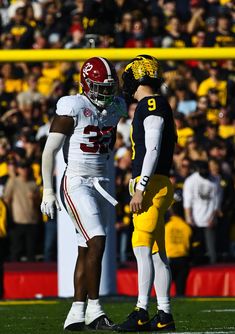 two football players standing next to each other on a field with fans in the stands