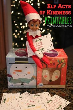 an elf sitting on top of a box next to some cards and a christmas tree