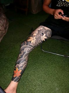 a person sitting in a chair with tattoos on their legs and leggings, holding a cell phone