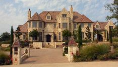 a large stone house with lots of trees and bushes around it's front entrance