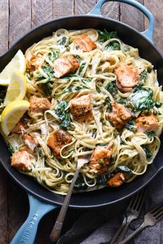 salmon and spinach pasta in a skillet with lemon wedges