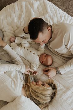 a man and woman are laying on a bed with their baby in the middle looking down at them