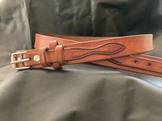 a pair of brown leather belts sitting on top of a black cloth covered bed sheet