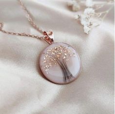 a necklace with a dandelion design on it sitting on top of a white cloth