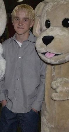 a young boy standing next to two large stuffed animals, one is smiling and the other has his hands in his pockets