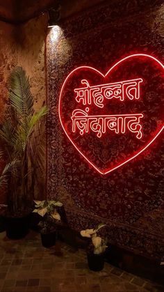 a heart shaped neon sign in front of a wall with plants and potted plants