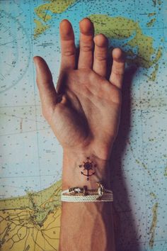 a person's hand with a small anchor tattoo on it, sitting in front of a map