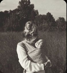 a woman holding a baby in her arms while standing in a field with tall grass