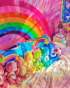 there are many stuffed animals on the bed with a rainbow theme in the back ground