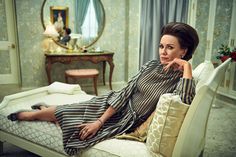 a woman sitting on top of a bed in a room with blue walls and curtains