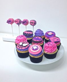 cupcakes with pink and purple frosting are arranged on a white platter