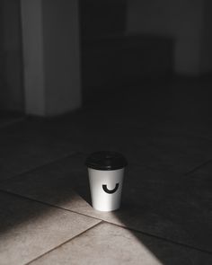 a coffee cup with a smiley face drawn on it's side sitting on the floor