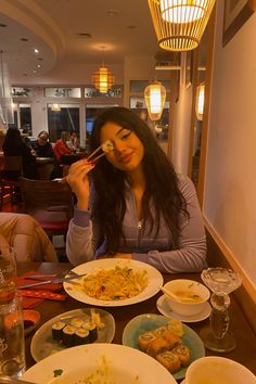 a woman sitting at a table with plates of food and chopsticks in her mouth