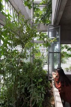 a woman sitting on a bench looking at her cell phone in an indoor garden area