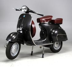 a black scooter with a red seat is parked on a white floor in front of a gray wall