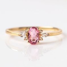 a pink diamond ring with three diamonds on the side and an oval shaped stone in the middle