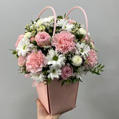 a hand holding a pink and white flower arrangement in a shopping bag with greenery