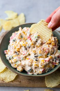 a hand dipping a chip into a bowl full of corn salad with chips on the side