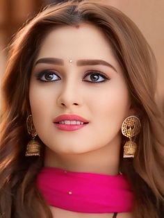 a woman with long brown hair wearing earrings and a pink dress is looking at the camera