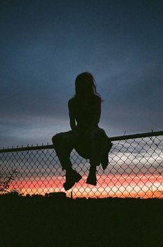 a woman sitting on top of a fence next to a fire hydrant at sunset