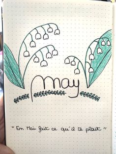 a hand holding a notebook with the word may written on it and lily of the valley flowers