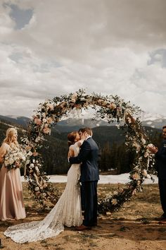 a bride and groom standing in front of a wedding arch with floral decorations on it