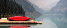 a red canoe sitting on top of a wooden dock in front of a mountain lake