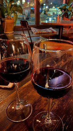 two glasses of red wine sitting on top of a wooden table next to each other