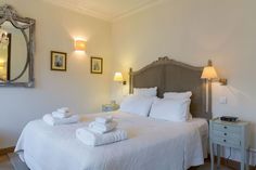 a bed with white linens and folded towels on it, in a room with two lamps