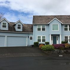 a blue house with two garages and bushes in front