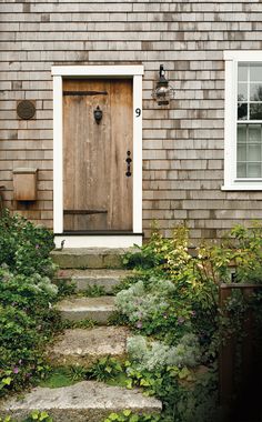 a house with a wooden door and steps leading up to the front door is surrounded by greenery