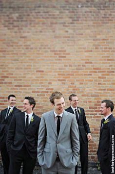 a group of men standing next to each other in front of a brick wall wearing suits and ties