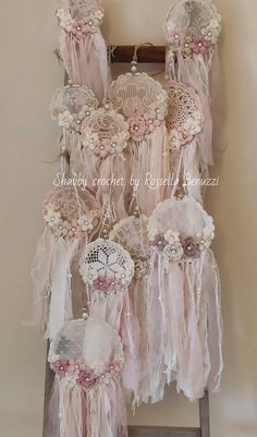 an old ladder is decorated with pink and white laces, crocheted doily, and flowers