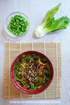 a bowl filled with green vegetables next to another bowl full of food on top of a bamboo mat