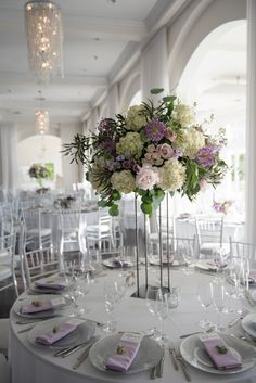 a tall vase filled with lots of flowers on top of a white table cloth covered table