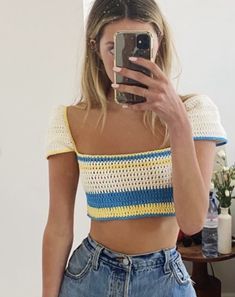 a woman taking a selfie with her cell phone in front of her, wearing jeans and a crop top