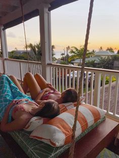 two women laying on a porch swing with the sun setting in the distance behind them