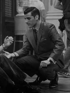 a man in a suit and tie sitting on the ground next to a woman who is holding her hand out