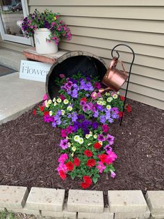 flowers are growing out of the ground in front of a flower pot with a watering can next to it