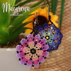 two beaded earrings are sitting in a white pot next to a plant and sunflower