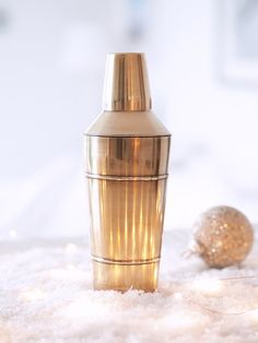 a gold cocktail shaker sitting on top of a pile of snow next to a christmas ornament