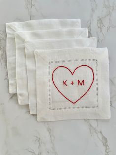 three white napkins with embroidered heart and m on the front one has a monogram