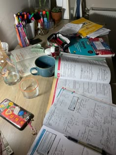 many papers and pens are on the table next to a cup with liquid in it